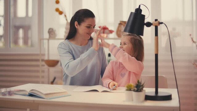 Friendly mom helping child with homework, giving high-five to daughter, teamwork