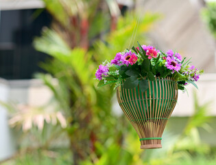 Multi-colored of fake flowers in the wooden basket  in the park with natural background at Thailand for design and decoration.