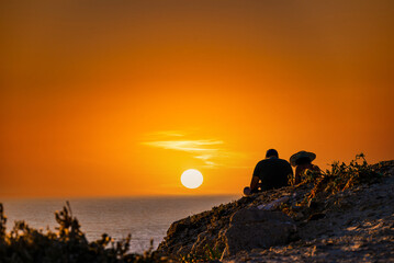 Naklejka na ściany i meble Young couple watching the sunset on the Barbate beach next to the Trafalgar lighthouse, Cádiz 