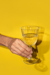Hand holding the white wine in a  glass on a yellow background