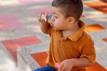 Young boy with Down syndrome blowing bubbles on the sidewalk in front of his house