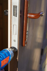 Handyman check door lock with screw gun in front door. Checking lock close up for operability in door.