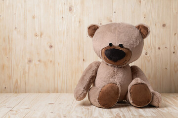 Cute teddy bear on table near wooden wall, space for text