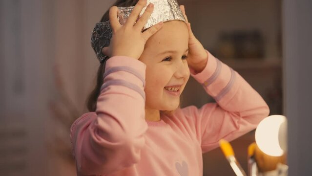 Smiling girl wearing foil crown and playing in front of mirror, little princess