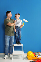 Father and son with roller near blue wall. Repair work