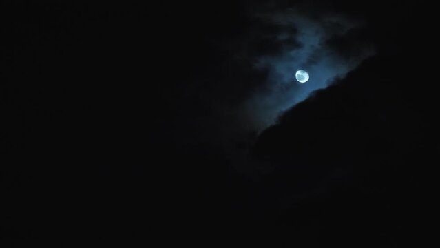 Beautiful full moon in the night sky. Gloomy black clouds move nearby. Mysterious and frightening view of the night sky through the window