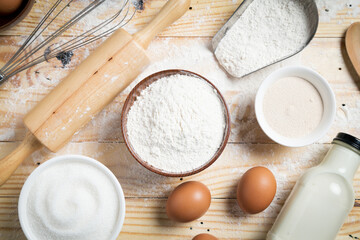 Homemade dough recipe (eggs, flour, milk, sugar) and kneaded dough on a wooden table. view from above