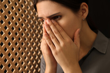 Upset woman covering face with hands and listening to priest during confession in booth, closeup