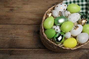 Many beautifully decorated Easter eggs in wicker basket on wooden table, above view. Space for text