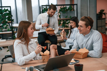 Talking, having a break. Group of coworkers are eating food from eco boxes in the office together