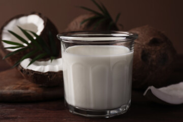 Glass of delicious vegan milk, coconut pieces and palm leaves on wooden table