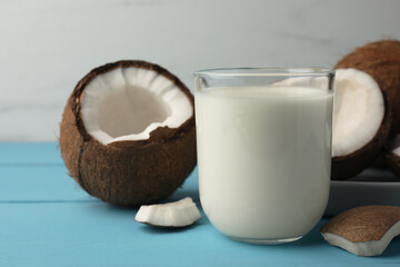 Glass of delicious vegan milk and coconuts on light blue wooden table