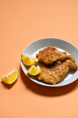 Classic fried Wiener Schnitzel served with lemon on a white plate. Breaded fried meat. A traditional dish of Austrian or German cuisine. Close-up. Copy space. Orange bright background