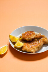 Classic fried Wiener Schnitzel served with lemon on a white plate. Breaded fried meat. A traditional dish of Austrian or German cuisine. Close-up. Copy space. Orange bright background