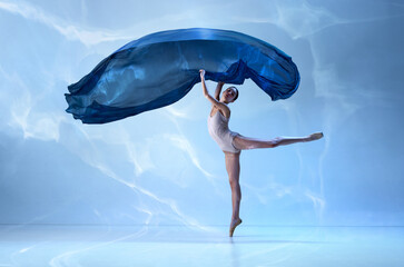 Graceful movements of one beautiful ballerina dancing with silk cloth isolated over blue background. Female dancer in ballet outfit © Lustre Art Group 