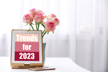 Trends For 2023 text on tablet display. Device, phone and flowers on white table, space for text