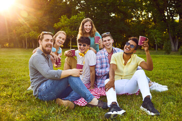 Company of young multicultural friends having fun drinking from paper cups sitting on green lawn in...