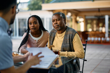 Black  senior man and his daughter communicating with healthcare worker on patio at residential care home.