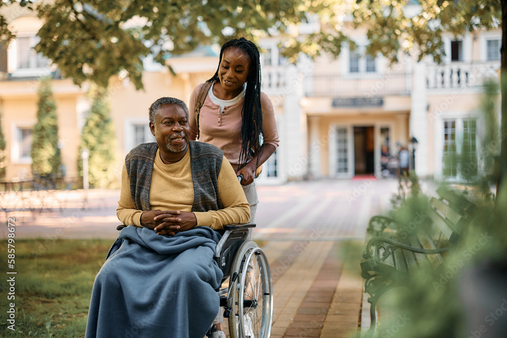 Wall mural happy black woman pushes her senior father in wheelchair while visiting his at nursing home.