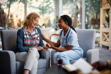 Caring black nurse consoling senior woman while talking to her in nursing home.