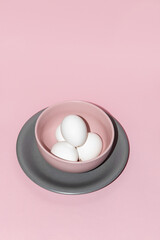 Fototapeta na wymiar White eggs in a pastel pink bowl on a gray plate over pink background