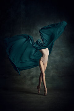Shot of tender professional ballerina dancing in beige bodysuit with fabric isolated over dark green background