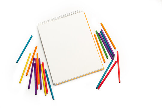 Cuaderno bloc junto a crayon de colores sobre un fondo blanco liso y aislado. Vista superior y de cerca. Copy space