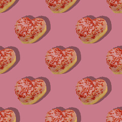 Pattern of heart shaped strawberry flavored donuts with shadow on pink background