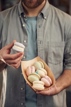 Man in casual clothes is holding macarons that are in the paper eco box. Close up view