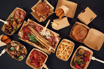 On the black colored table. Top view of food on it. Meat, vegetables, French fries, burger, mushrooms