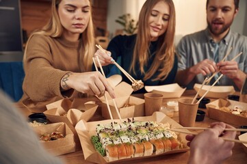 Using chopsticks. Friends are sitting indoors at home and eating sushi together