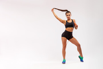 Fototapeta premium Beautiful fitness woman, cheerful and looking into the camera, isolated against a gray background. Woman in sportswear relaxing after a workout at the gym. Happy athletic girl