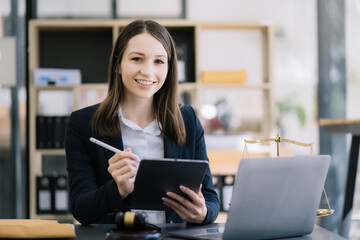 Justice and law concept. Female judge in a courtroom with the gavel working with digital tablet computer docking keyboard on wood table.