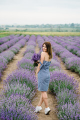 Girl standing back in a lavender flowers field. A beautiful woman walk on the lavender field. Enjoy the floral glade, summer nature. Natural cosmetics concept. Female collect lavender. Back view.