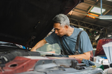 Fototapeta na wymiar Concentrated technician and experienced car engine repair specialist, Confident Asian man auto mechanic working in automobile repair garage, industrial business of maintenance workshop service