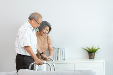 Elderly health insurance, Asian woman support senior older man walk at home, help and take care of elderly mature patient to doing physical therapy with walker for body health in house living room
