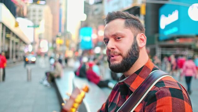 Musician is sitting and singing in New York city while playing a guitar.