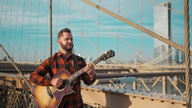 Musician singing on a bridge in New York city while playing a guitar.