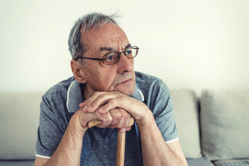 Shot of a senior man leaning in his walking stick at home. Hands of a thoughtful old man leaning on a cane, sitting at home.