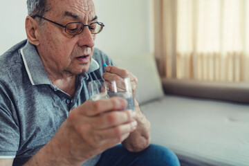 Senior man takes pill with glass of water in hand. Stressed mature man drinking sedated antidepressant meds. Man feels depressed, taking drugs.
