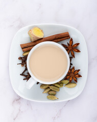 Obraz na płótnie Canvas White cup with masala chai on a saucer and cinnamon, anise with cloves and ginger root with cardamom.