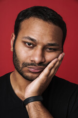 Bored indian man propping his head and looking at camera isolated over red background