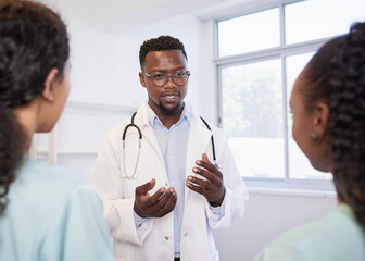 Senior doctor talks to junior healthcare assistants, standing team in hospital