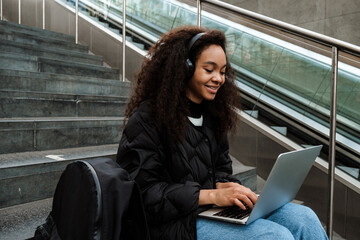 Fototapeta premium Young african girl working on laptop while sitting on stairs