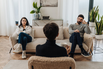 Married couple sitting on opposite sides of couch during therapy session with psychologist - obrazy, fototapety, plakaty