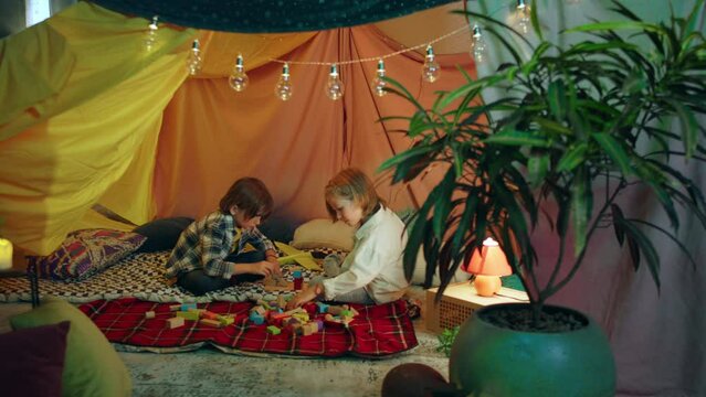Two children sitting down with each other are talking and enjoying themselves while playing together inside a sheet tent