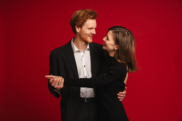 Beautiful couple hugging and looking at each other while standing isolated over red wall
