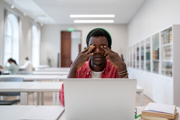 Eye strain and virtual learning. Tired African American guy university student sitting at desk with...
