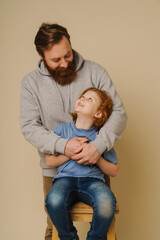 Father and son smiling and hugging isolated over beige background