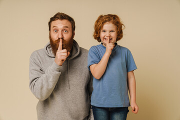 Ginger father and son showing silence gesture and looking at camera isolated